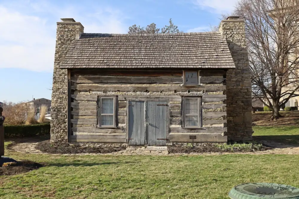 Photograph of a restored two-storey log house with stone chimney